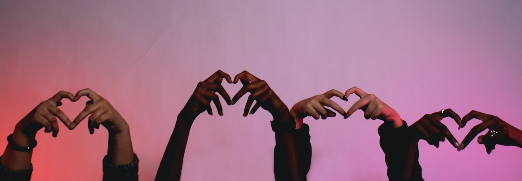 Four sets of hands forming hearts on a pinkish background