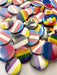 An assortment of round buttons with different Pride flags on them are scattered across a white background.