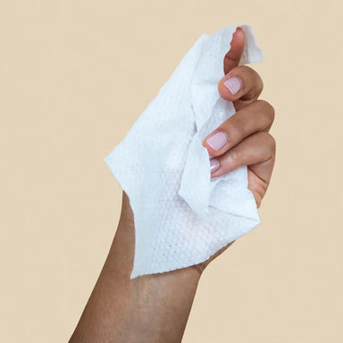Hand holding a dame wipe in front of a light peach background