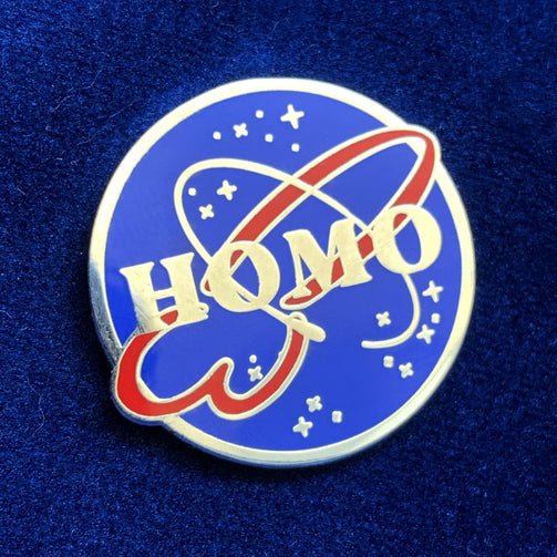 A silver-plated enamel pin that looks like the NASA logo but instead of NASA it says HOMO. The logo has a silver outline on a light blue circle. A red swirly design that is shaped like a penis and a finer circular line that looks like the ring of a planet surround the word HOMO. Twinkling stars of various sizes also surround the logo.