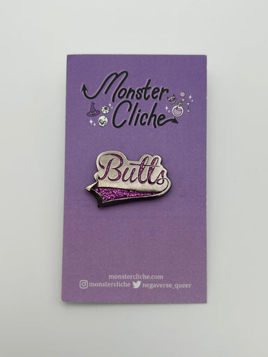 The Butts pin is attached to the card backing that it comes on, a purple card that says Monster Cliché at the top and the website and social media for the artist at the bottom. Website: monstercliche.com Instagram: @monstercliche Twitter: @megaverse_queer