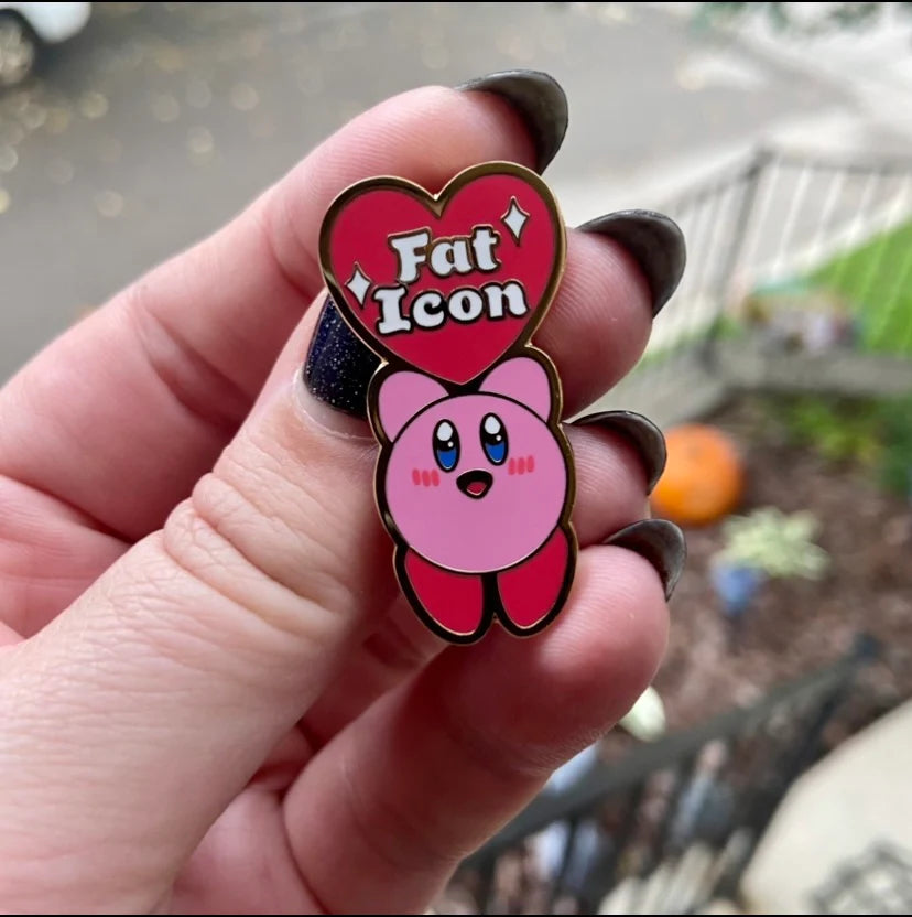 Enamel pin of kirby holding up a heart that says Fat Icon in the middle, with sparkles surrounding the words. 