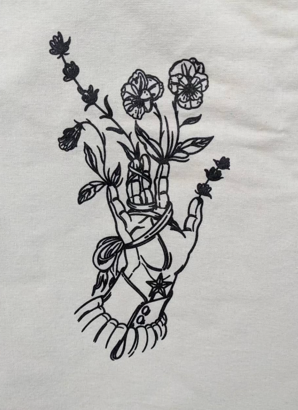 White tote bag with black floral design hanging on a brick wall