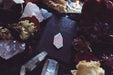 The crystal pin is pictured on the Grrrl Spells card that is comes on. The card is black with a grrrl spells logo. The pin is on a blanket, surrounded by crystals and dried flowers, and a tea light candle. 