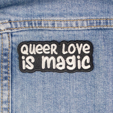 A simple patch with a black background and white text that reads "Queer Love is Magic".