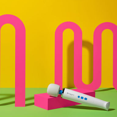 Magic wand mini resting on pink neon box, with a neon pink, yellow and green background