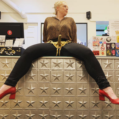 Woman sitting on a counter wearing a harness with gold Leo inside