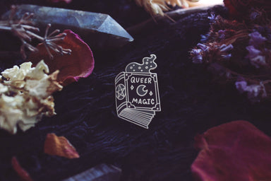 Queer magic pin surrounded by flowers and crystals