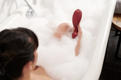 person in a bath holding the womanizer duo above bubbles